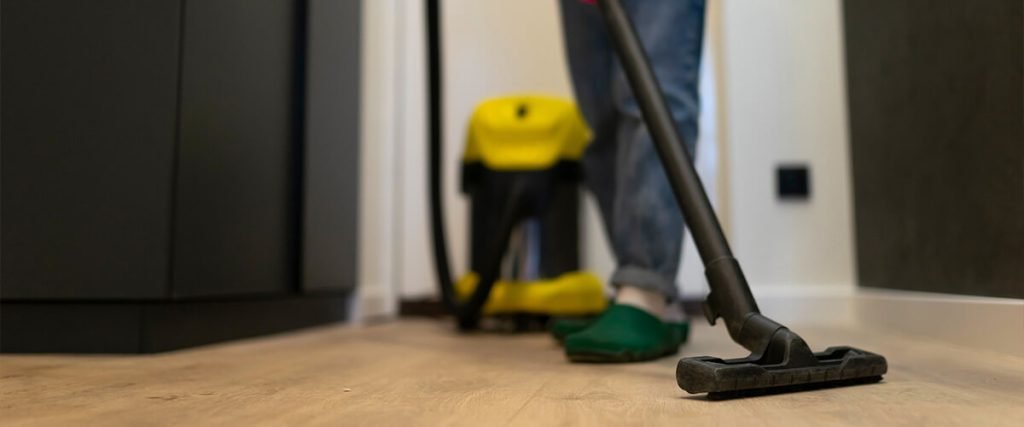 Personne aspirant un sol en bois avec un aspirateur de chantier jaune en arrière-plan
